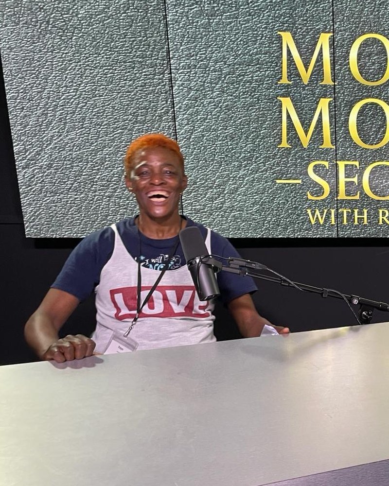 Adedayo laughing behind a studio microphone during a podcast recording.